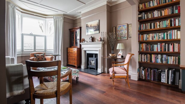 A well-lit room with a fireplace, a bookshelf, and a piano. - Caithness Road VI by Onefinestay (London)
