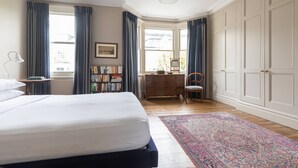 A bedroom with a large bed, a desk, a chair, a bookshelf, and a wardrobe. - Caithness Road VI by Onefinestay (London)