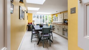 A modern kitchen with a large dining table, chairs, and a view of the outdoors through skylights. - Caithness Road VI by Onefinestay (London)