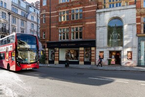 A red double-decker bus on a city street. - Culford Gardens III by Onefinestay (London)