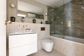 A modern bathroom with a glass-enclosed shower, a white toilet, and a vanity with a mirror and plants. - Culford Gardens III by Onefinestay (London)