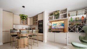 A modern kitchen with a dining area, a television, and a bar area with shelves. - Culford Gardens III by Onefinestay (London)