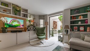 A modern living room with a flat-screen TV, a green chair, a sofa, and a dining area with chairs and a table. - Culford Gardens III by Onefinestay (London)