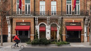 A brick building with storefronts labeled "Cartier" and a cyclist on the sidewalk. - Culford Gardens III by Onefinestay (London)