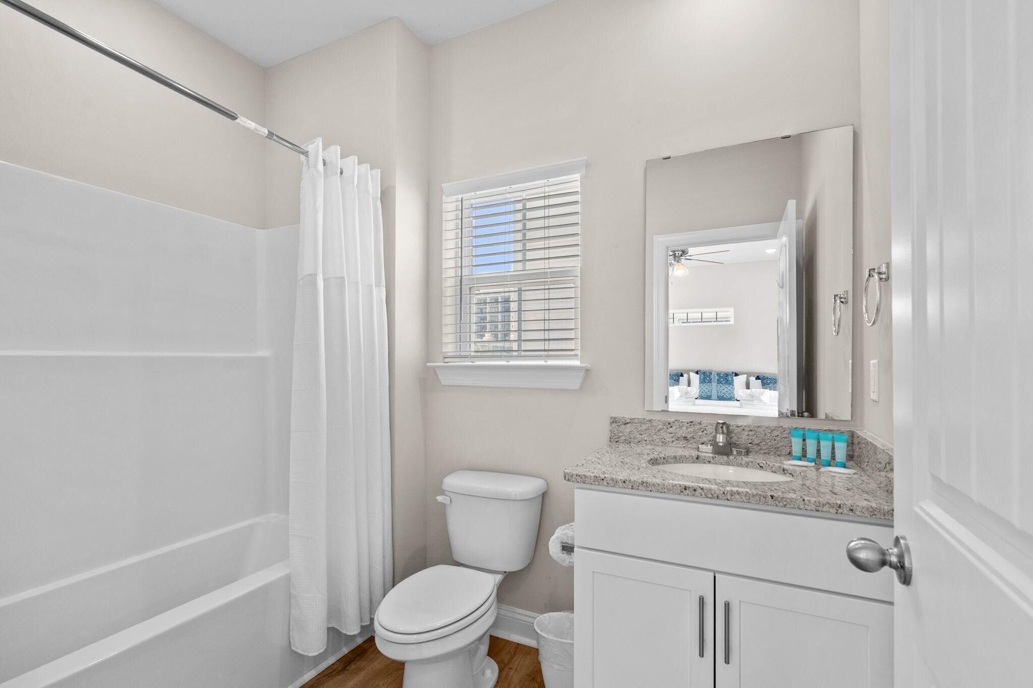 Baño con ducha, inodoro, lavamanos y ventana con persianas.