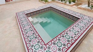 A spacious courtyard with a decorative pool, a staircase, and a seating area with cushions. - Riad Solila (Marrakech)