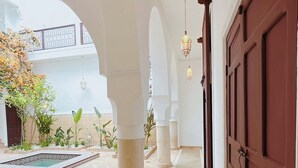 A corridor with a tiled floor, columns, and a large wooden door. - Riad Solila (Marrakech)