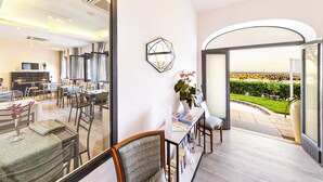 A modern hotel room with a dining area, a piano, and a view of a landscaped garden. - Hotiday Room Collection - Massa Lubrense (Massa Lubrense)
