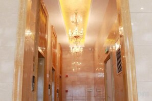 Un couloir orné d’un lustre, avec un ascenseur et une porte au fond.