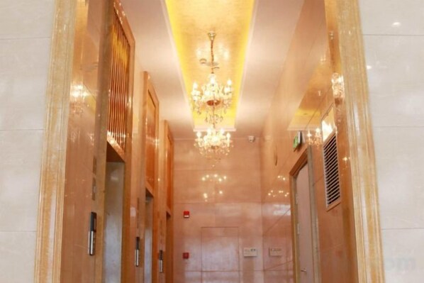 Un couloir orné d’un lustre, avec un ascenseur et une porte au fond.