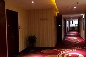 A hotel corridor with a red carpet, a potted plant, and a door on the left. - Zhoushan Perfect Business Hotel (Zhoushan)