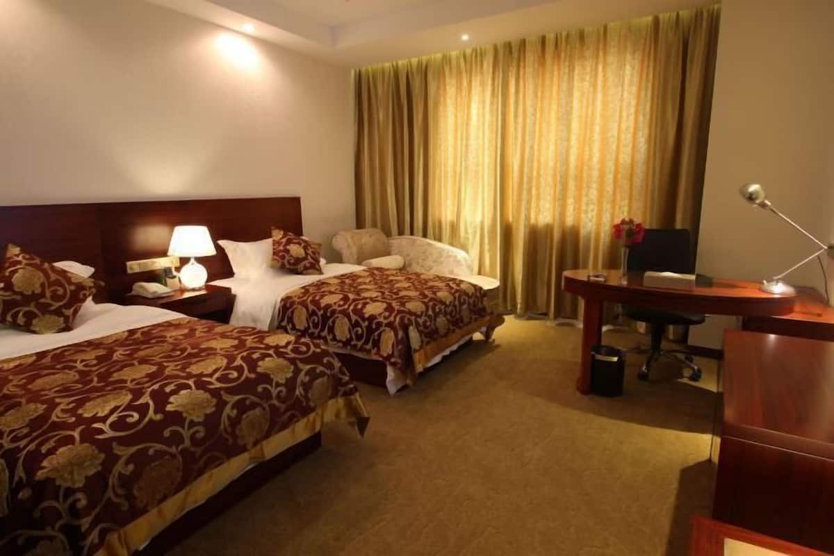 A hotel room with two beds, a desk, a chair, a lamp, and a curtain.