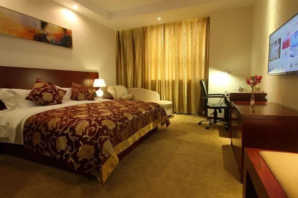 A hotel room with a bed, a desk, a chair, a lamp, a television, and a large window with curtains.
