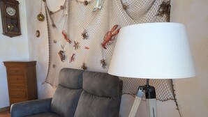 Ein Wohnzimmer mit grauem Sofa, einer Stehlampe, einer Holzkommode und einer Wand mit einer Netzdeko mit Meereslebewesen.