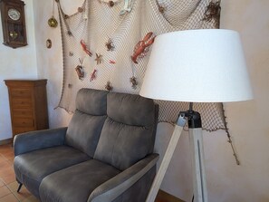 Una sala de estar con un sofá gris, una lámpara de pie, un aparador de madera y una pared decorada con una red que muestra criaturas marinas.