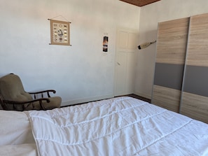 A bedroom with a bed, a chair, a wardrobe, and a wall with a poster.