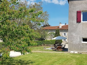 Una casa de piedra con una persiana roja, césped y un patio con mobiliario de exterior.