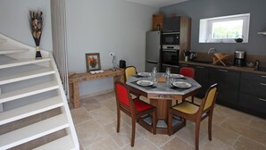 A modern kitchen with a dining area, including a wooden table and chairs, a built-in oven, and a window providing natural light. - Charming cottage in the heart of the Vosges (Removille)