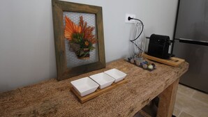 A kitchen counter with a framed floral artwork, a coffee machine, and three white bowls on a wooden tray. - Charming cottage in the heart of the Vosges (Removille)