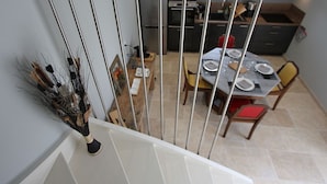 A dining area with a table set for four, a kitchen in the background, and a staircase leading to another floor. - Charming cottage in the heart of the Vosges (Removille)