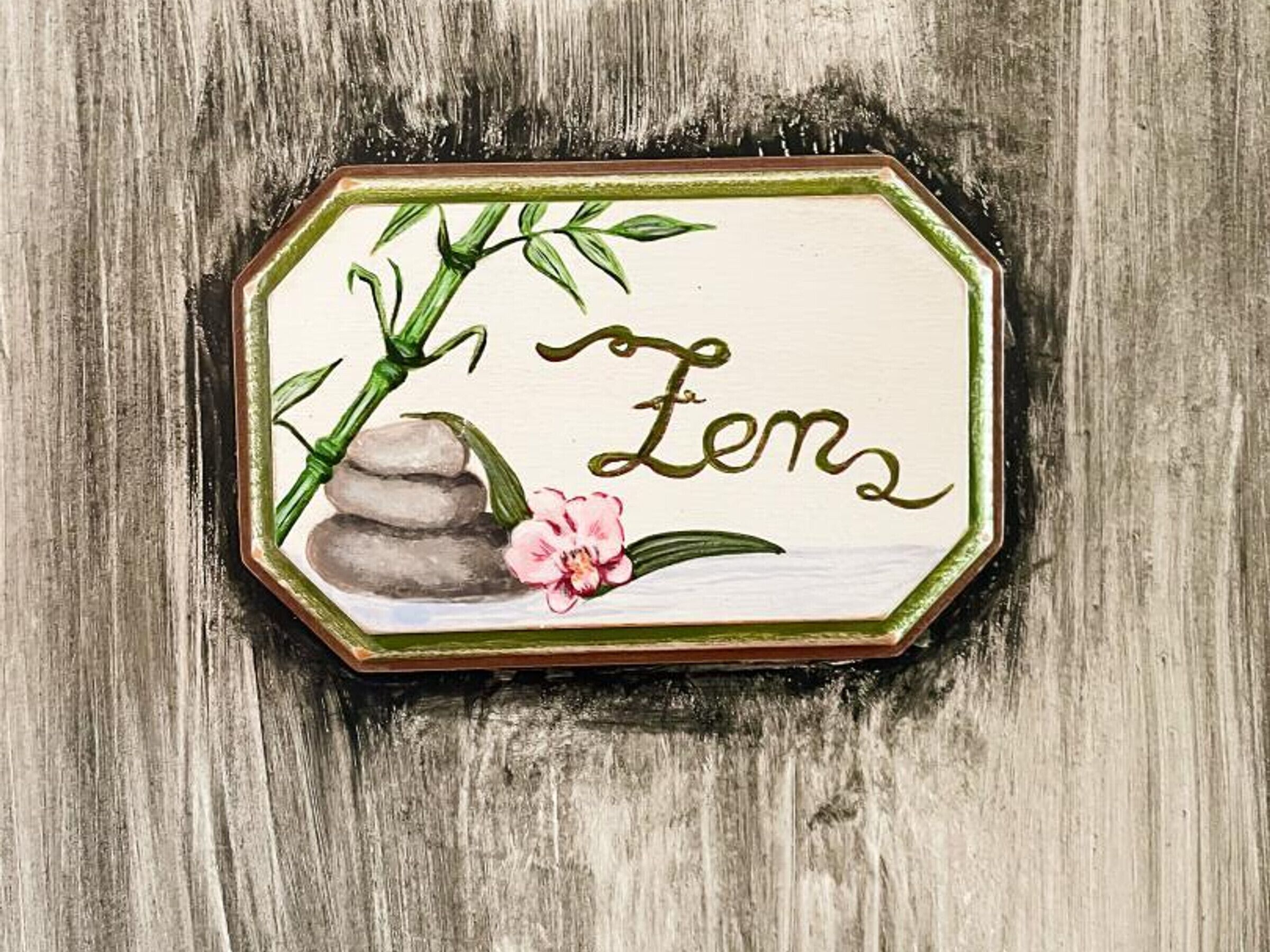 Un segnale di legno con un motivo decorativo raffigurante un ramo di bambù, una pila di pietre e un fiore rosa.