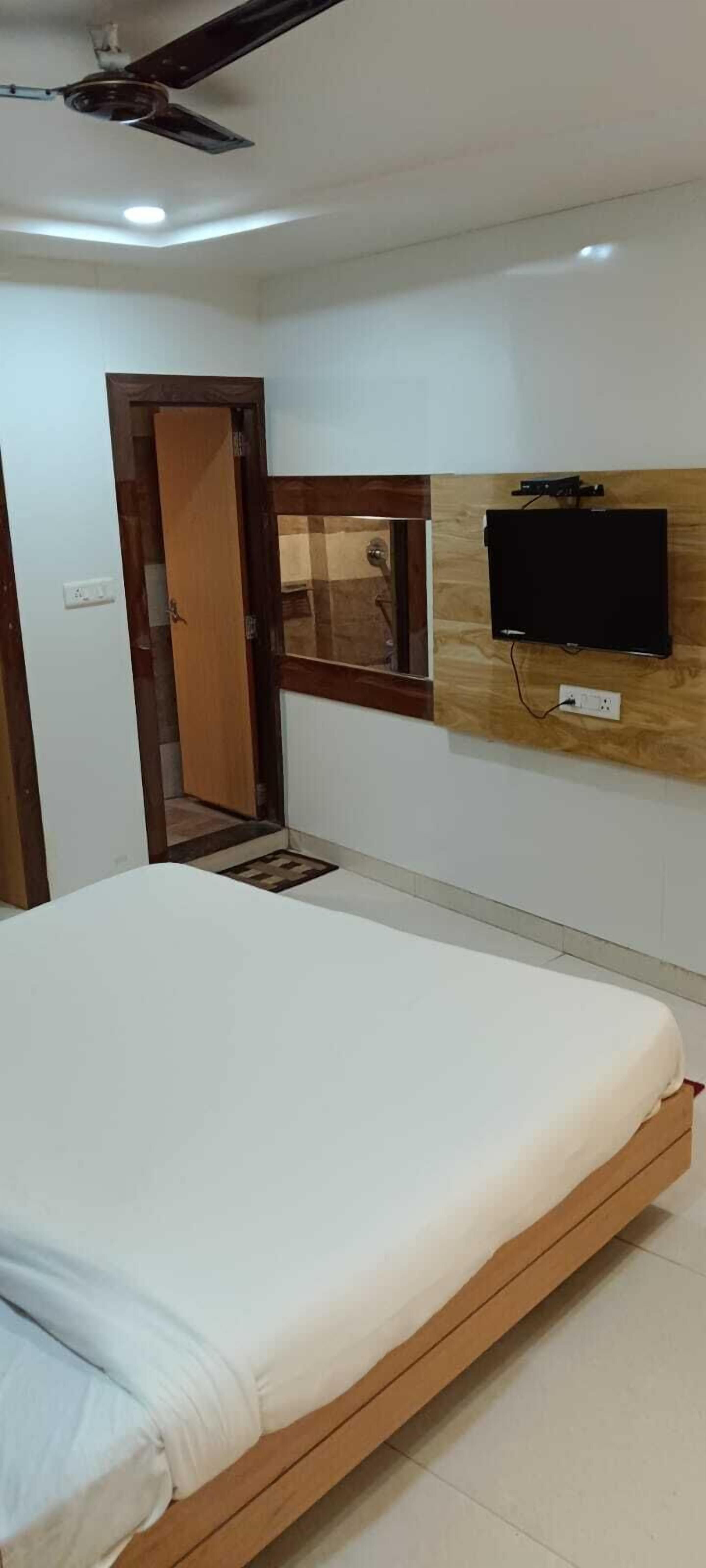 A bedroom with a bed, a TV mounted on the wall, and a ceiling fan.