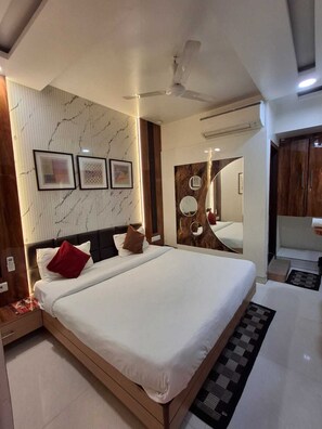 A modern bedroom with a large bed, a ceiling fan, and a mirror above the bed. - Hotel Sapphire Inn (Gorakhpur)
