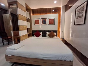 A modern hotel room with a large bed, a wooden wardrobe, and a desk with a chair. There are three framed pictures on the wall above the bed. - Hotel Sapphire Inn (Gorakhpur)