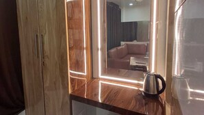 A room with a wooden wardrobe, a mirrored vanity with LED lights, a coffee maker, and a chair. - Hotel Sapphire Inn (Gorakhpur)