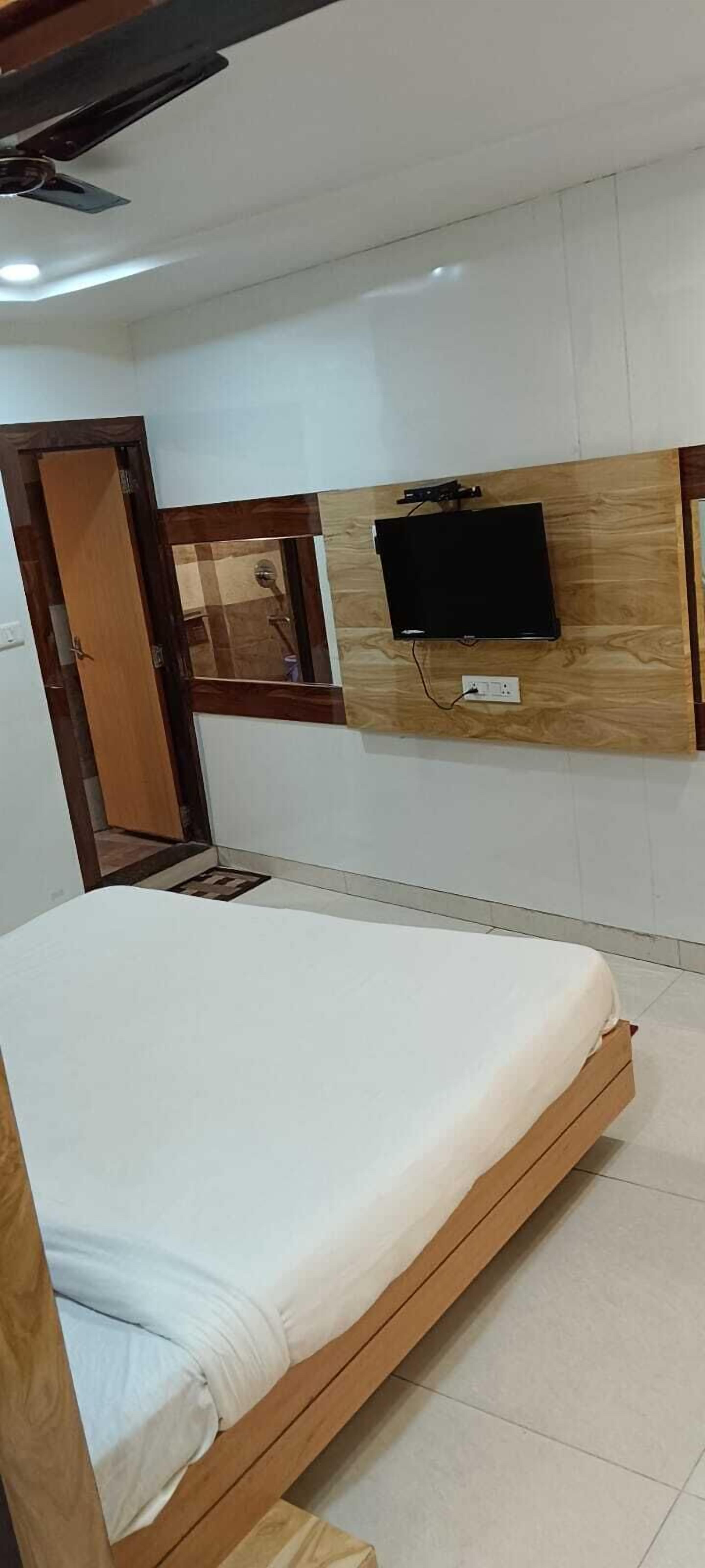 Un dormitorio con cama, televisión instalada en la pared y armario de madera.