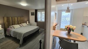 Une chambre à coucher avec un lit, une table de chevet et une fenêtre avec des rideaux. Il y a également un coin repas avec une table et des chaises.