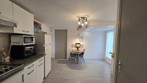 Une cuisine compacte dotée d’appareils électroménagers modernes, un coin repas avec une table et des chaises, et une grande fenêtre qui laisse entrer la lumière naturelle.