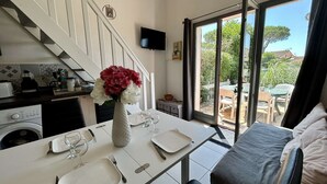 Un comedor con una mesa preparada para dos, una lavadora, un televisor montado en la pared y vistas al patio exterior.