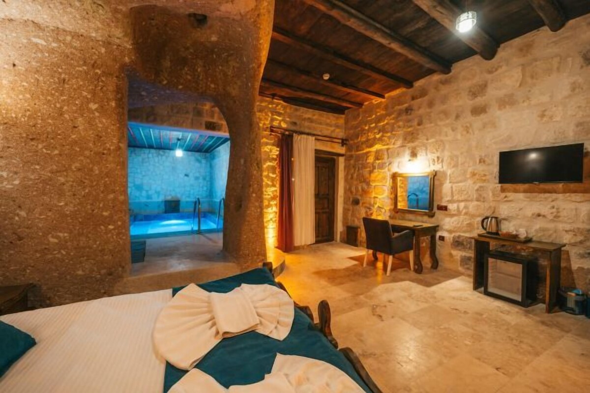 A rustic stone-walled room with a bed, a television, and a fireplace.