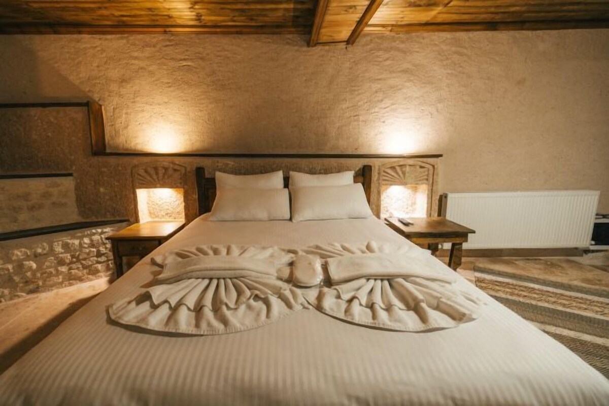 A bed with a decorative headboard, two bedside tables with lamps, and a stone wall.