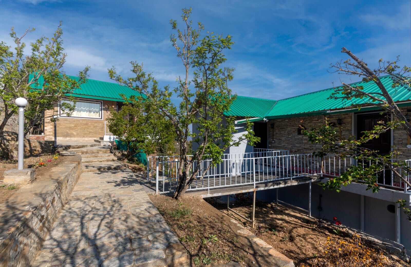 A building with a green roof, stone walls, and a paved pathway leading to a gated entrance.