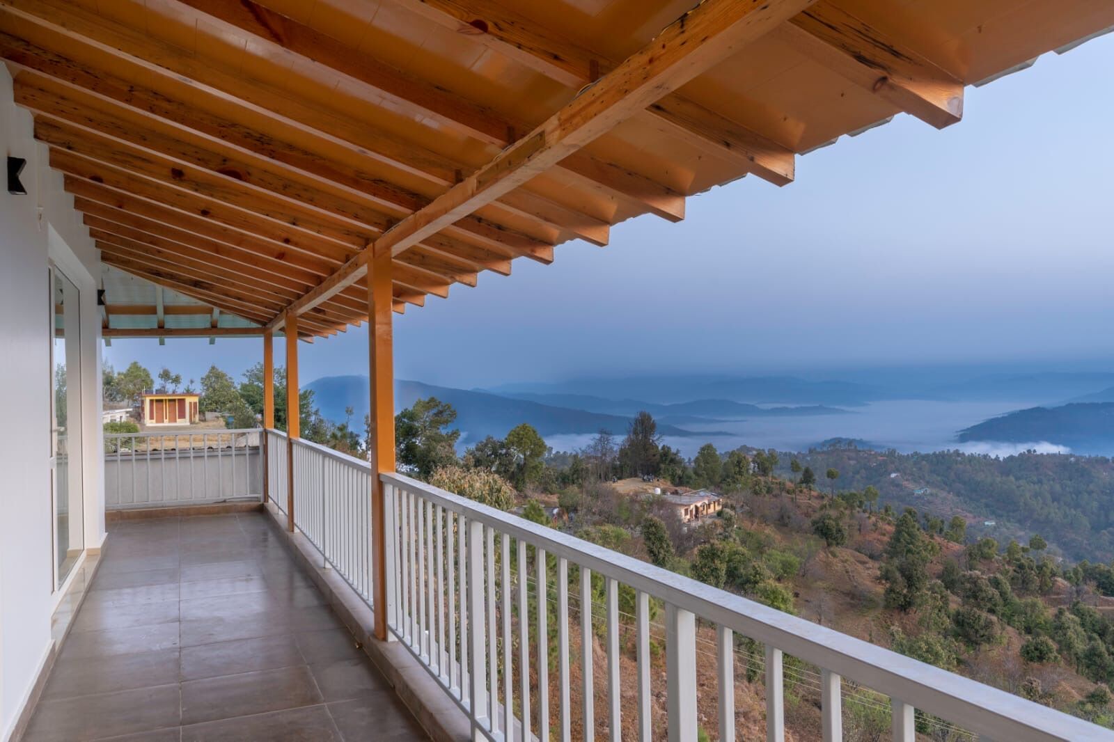 A covered balcony with a view of a mountainous landscape and a body of water.
