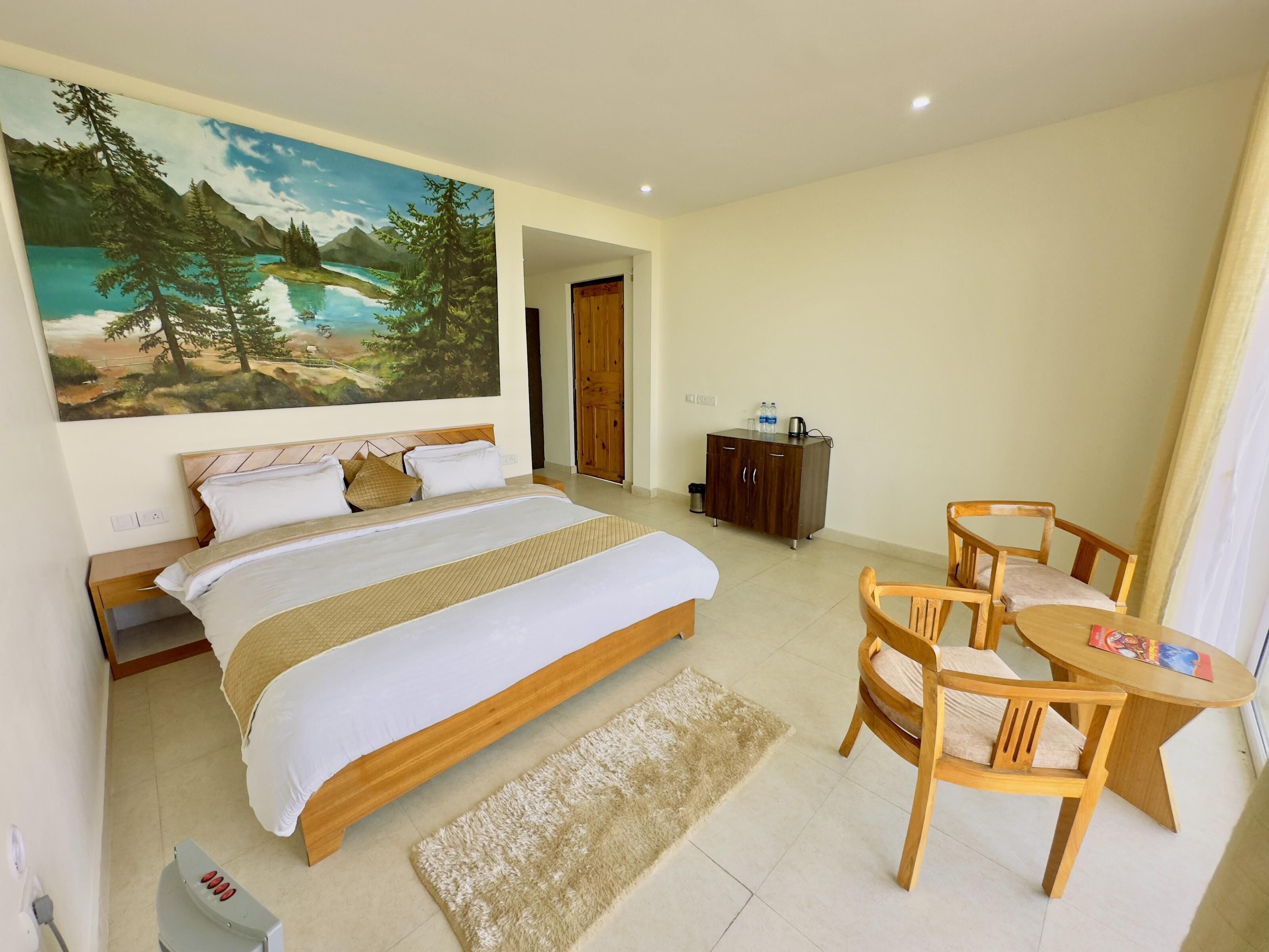 Ein Hotelzimmer mit einem großen Bett, einem Holztisch, zwei Stühlen, einer kleinen Kommode und einem Bild an der Wand.