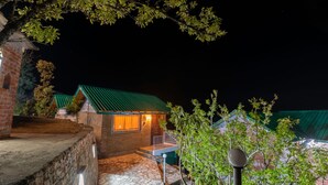 Un sendero de piedra que conduce a un edificio con techo verde y una ventana iluminada, rodeado de árboles.