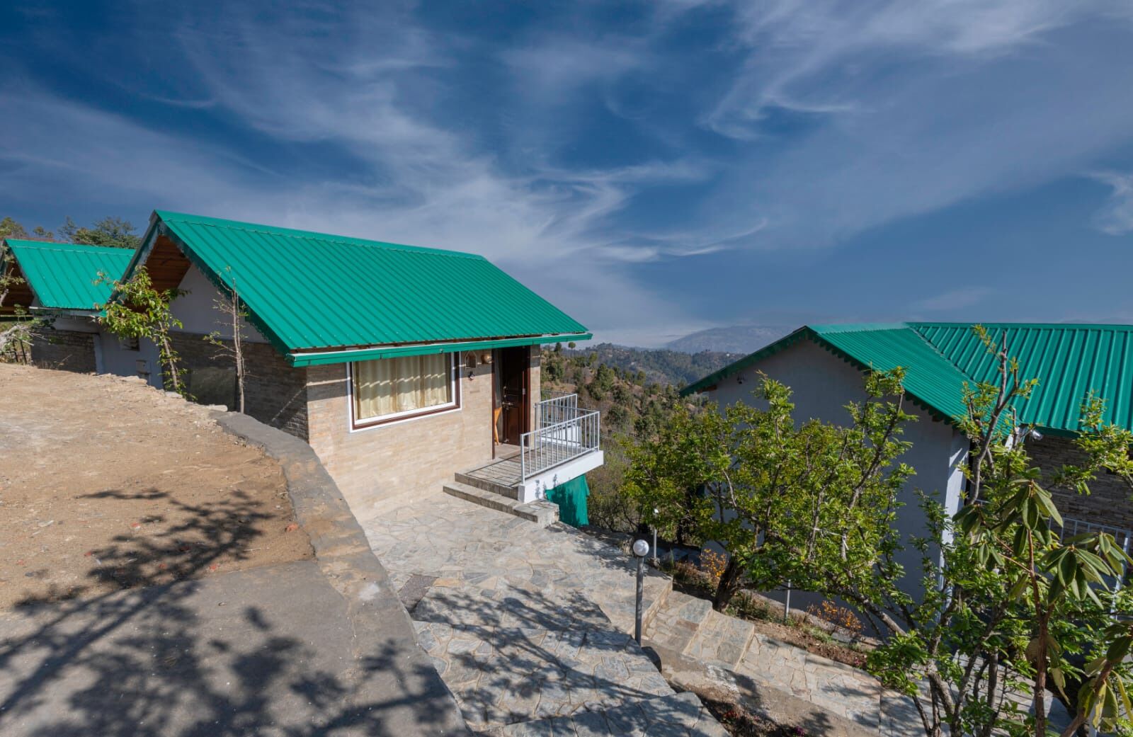 A hillside property with multiple buildings, each featuring a green roof and stone walls.
