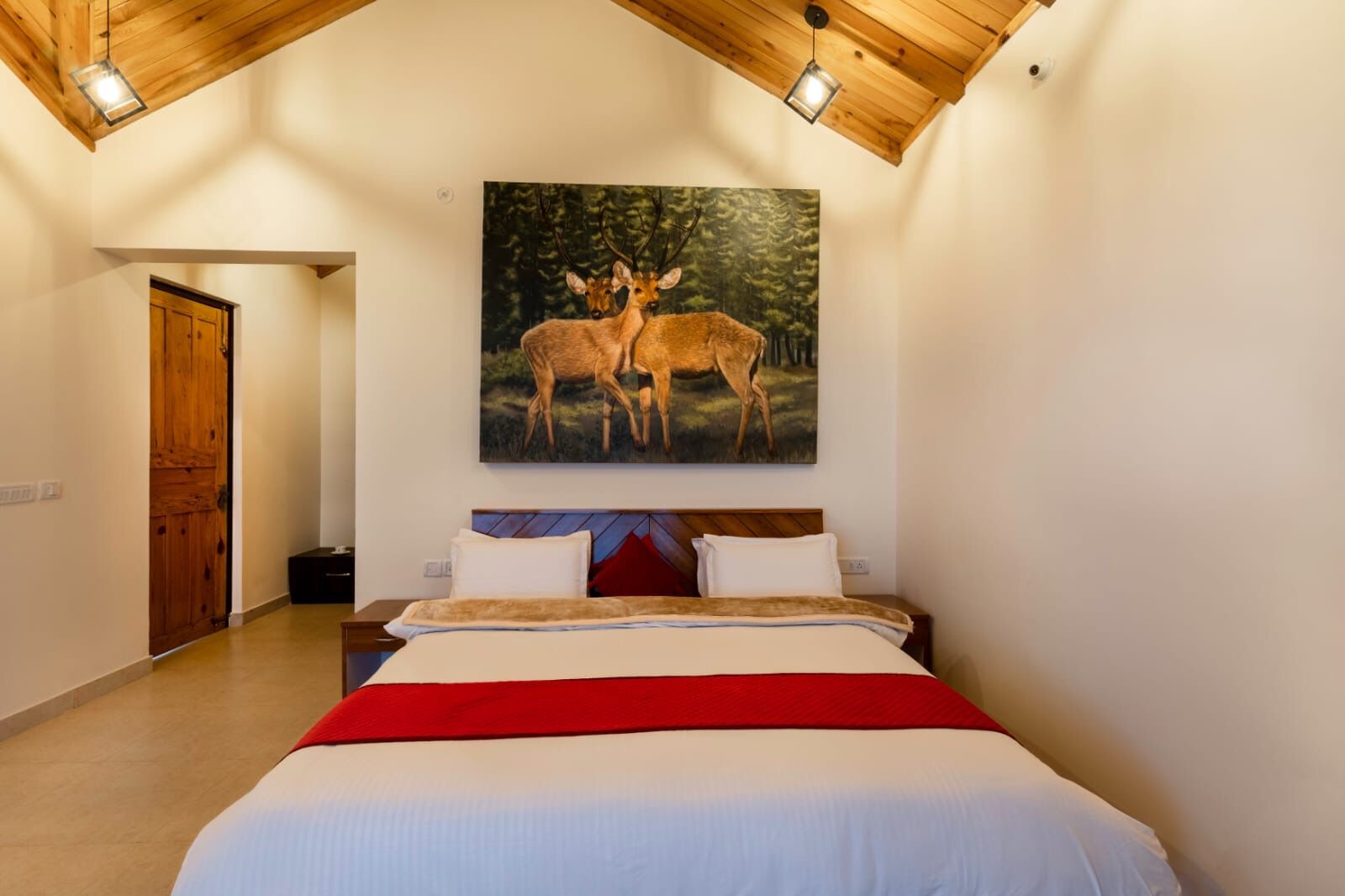 Une chambre avec un grand lit, un plafond en bois et un tableau représentant des cerfs accroché au mur.