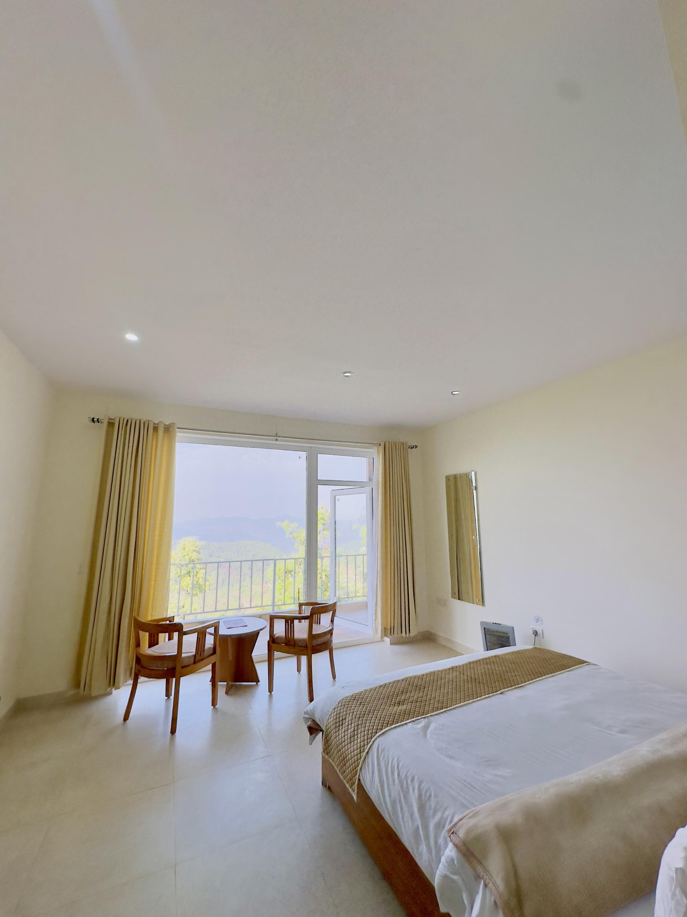 Een hotelkamer met een groot bed, een klein tafeltje met stoelen, een raam met gordijnen en een balkon.