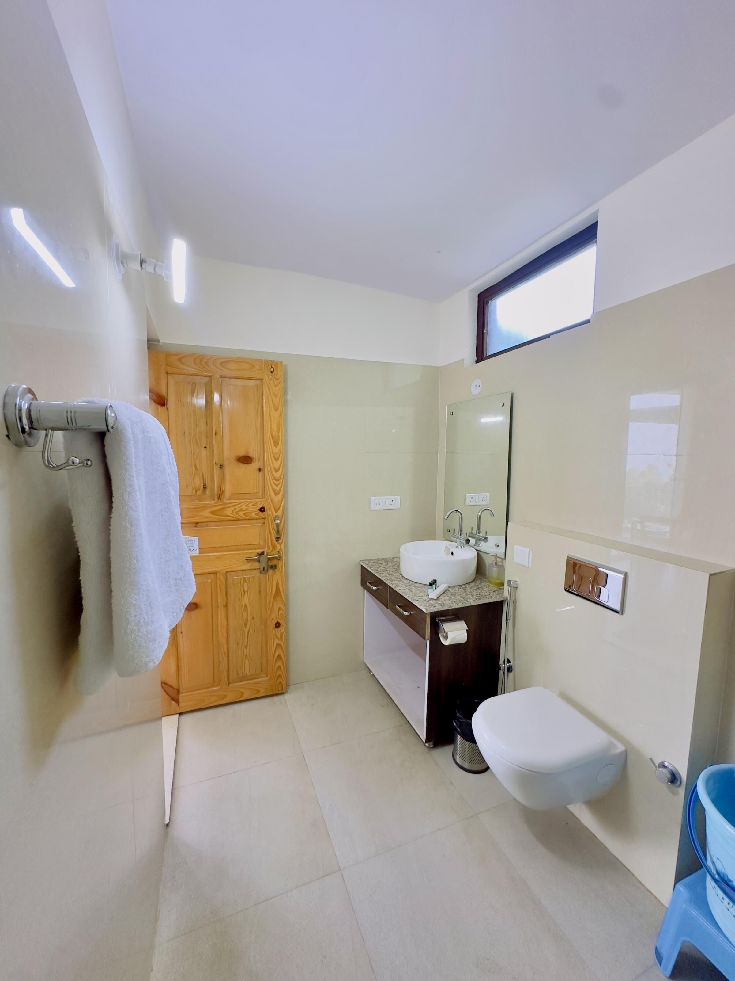 Um banheiro moderno com porta de madeira, pia com espelho e vaso sanitário.