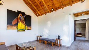 Una habitación amplia con un alto techo de madera, una mesa de centro de vidrio, un banco y dos cuadros en la pared.