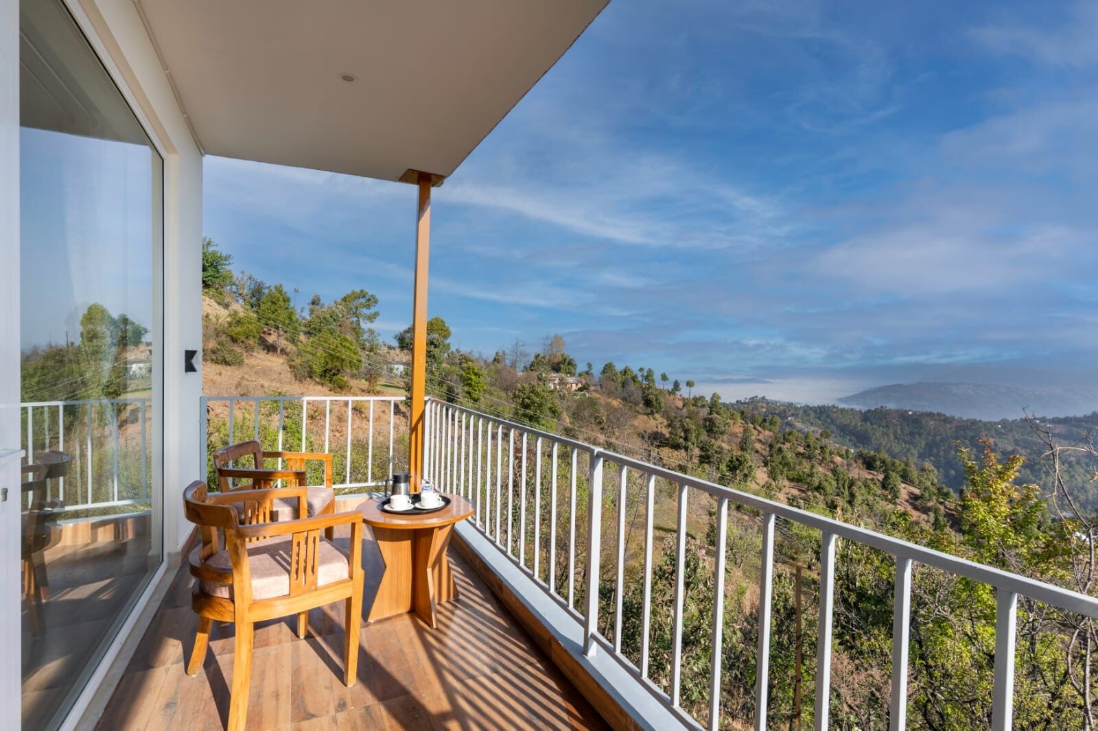 A balcony with a wooden table and chairs, overlooking a hilly landscape.