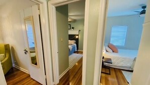 Un couloir étroit mène à une chambre à coucher qui contient un lit, une table de chevet et un ventilateur de plafond.
