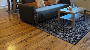 Un ampio soggiorno con pavimento in legno, un divano con cuscini, un tavolino da caffè e due lampade a sospensione.
