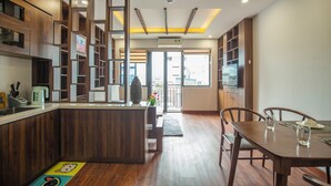 A modern kitchen with wooden cabinetry, a central island, and a dining area with a table and chairs. - Sumitomo7- Linh Lang Serviced Apartment (Hanoi)