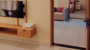 Une chambre d’hôtel dotée d’un téléviseur à écran plat fixé au mur, d’une console en bois sur laquelle est posée une serviette, et d’un lit avec une tête de lit blanche.