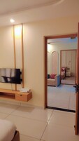 A hotel room with a flat-screen TV mounted on the wall, a wooden console table with a towel, and a bed with a white headboard.